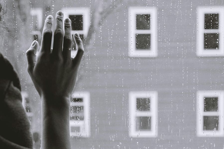 B&W image of a woman holding hand on rainy window.